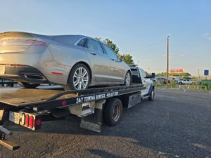 White flatbed tow truck hauling a silver sedan near a Fort Worth oil change shop, representing 24/7 emergency towing services.