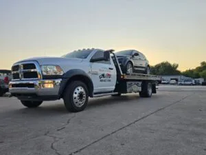 Front three-quarter view of a Quick & Slick Towing heavy-duty flatbed truck carrying a silver sedan, displaying the business logo and Fort Worth contact information for local roadside assistance.